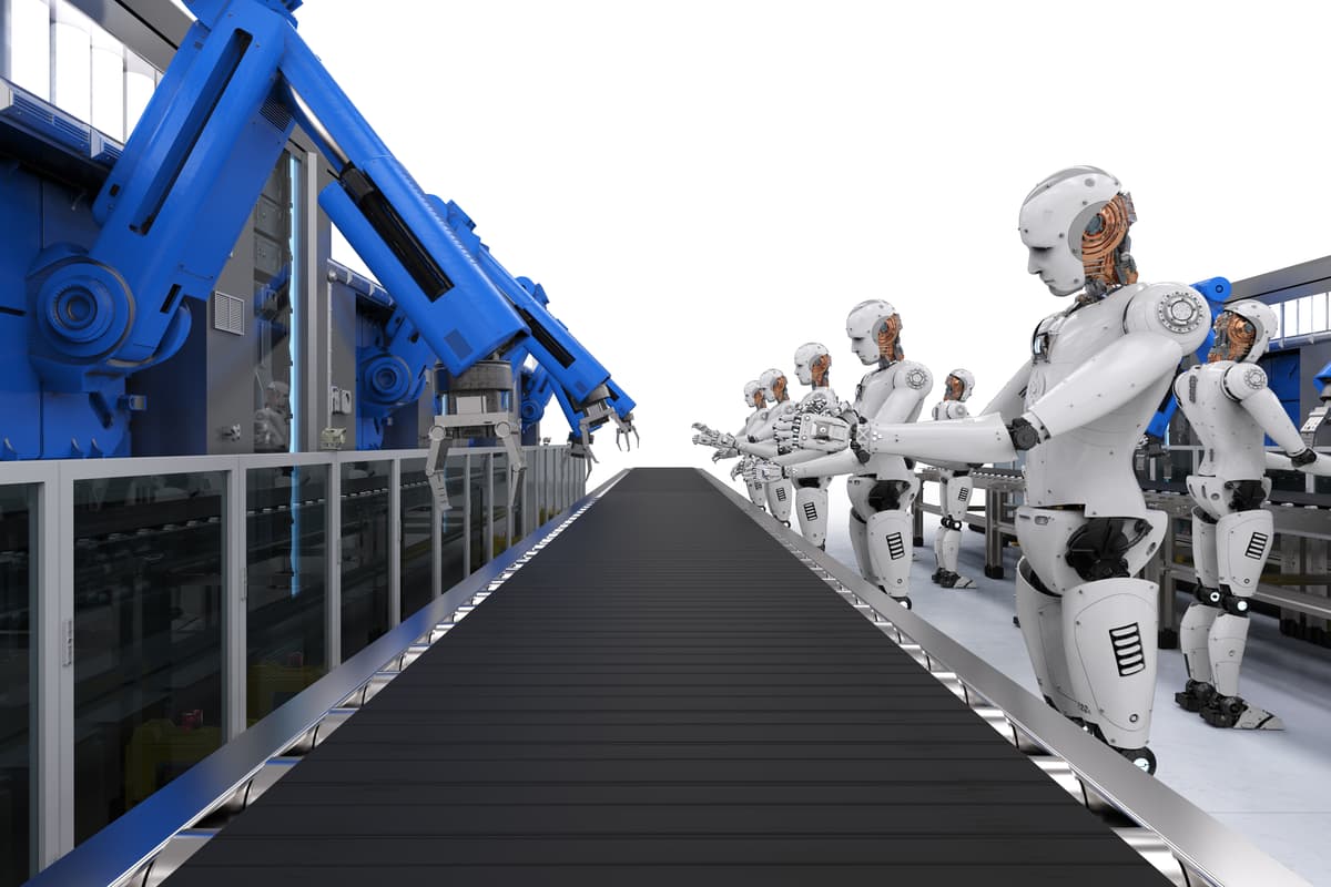 Robots with humanoid features stand beside a conveyor belt in a modern, high-tech factory, while large blue robotic arms work on the opposite side. | Betechit.com