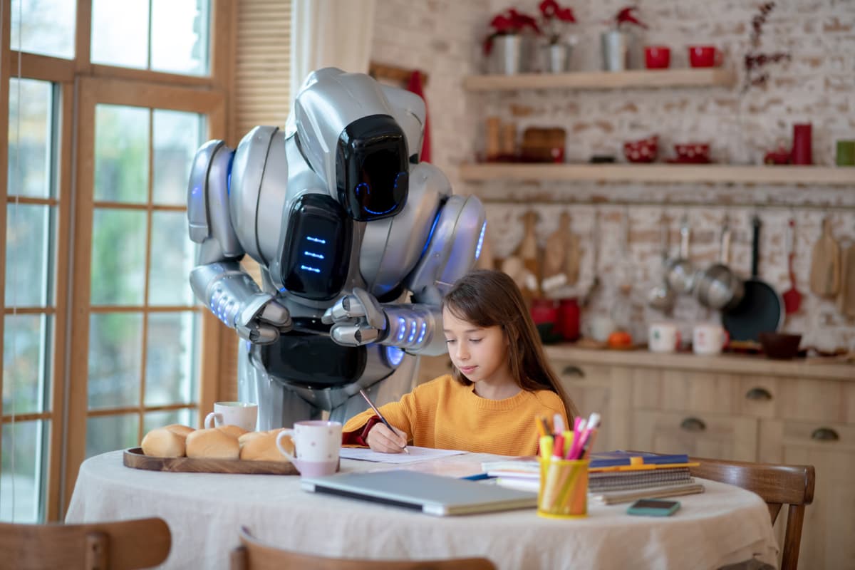 A robot stands behind a young girl who is writing at a kitchen table, surrounded by books and school supplies. The kitchen is cozy with bread on the table and pots hanging on the wall. | Betechit.com