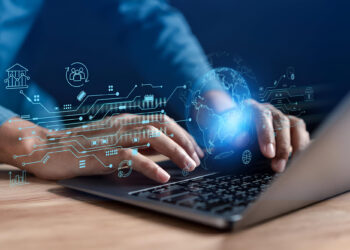 Person typing on a laptop with digital graphics showing technology, global connections, and financial icons overlaying the scene, symbolizing business technology and data transfer. | Betechit.com