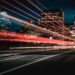 A city street at night with light trails from passing vehicles, surrounded by tall illuminated buildings. The sky is dark, highlighting the vibrant energy of urban life. | Betechit.com